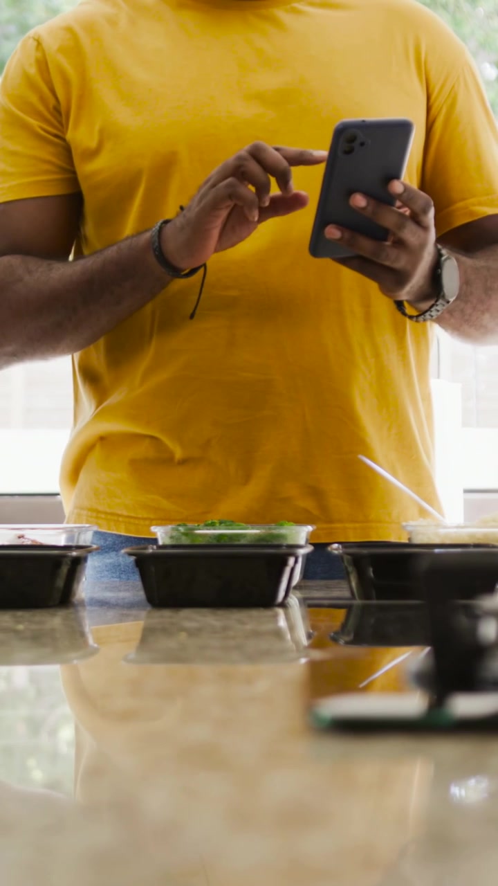 Vertical video: Unlocking phone, man yellow tee scrolling then calling in kitchen with 3 tubs