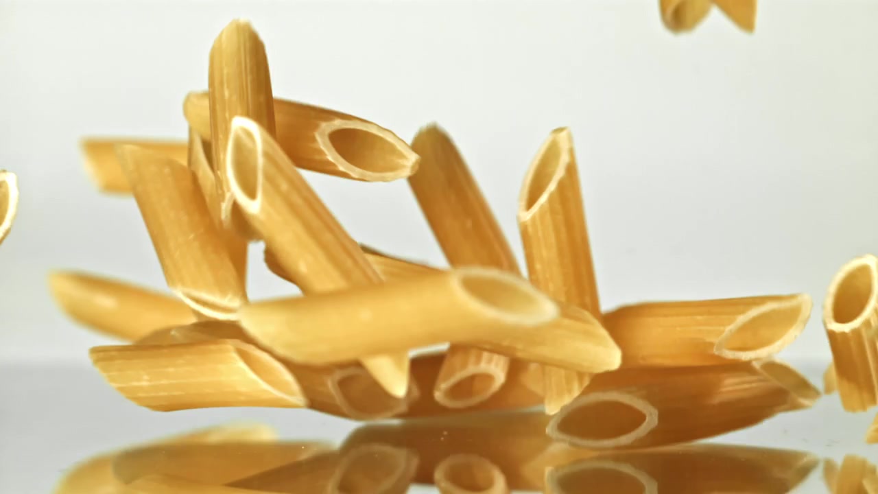 Pasta penne secca che cade al rallentatore su sfondo bianco