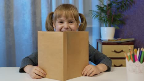 child girl looking at web camera making video call learning, studying at home, reading book, smiling