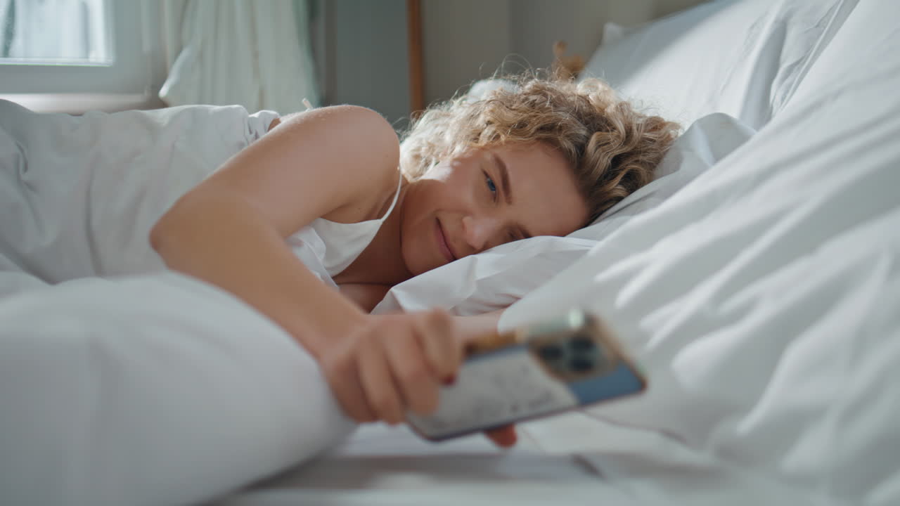 Sleepy girl checking smartphone in bed. Closeup peaceful woman waking up morning