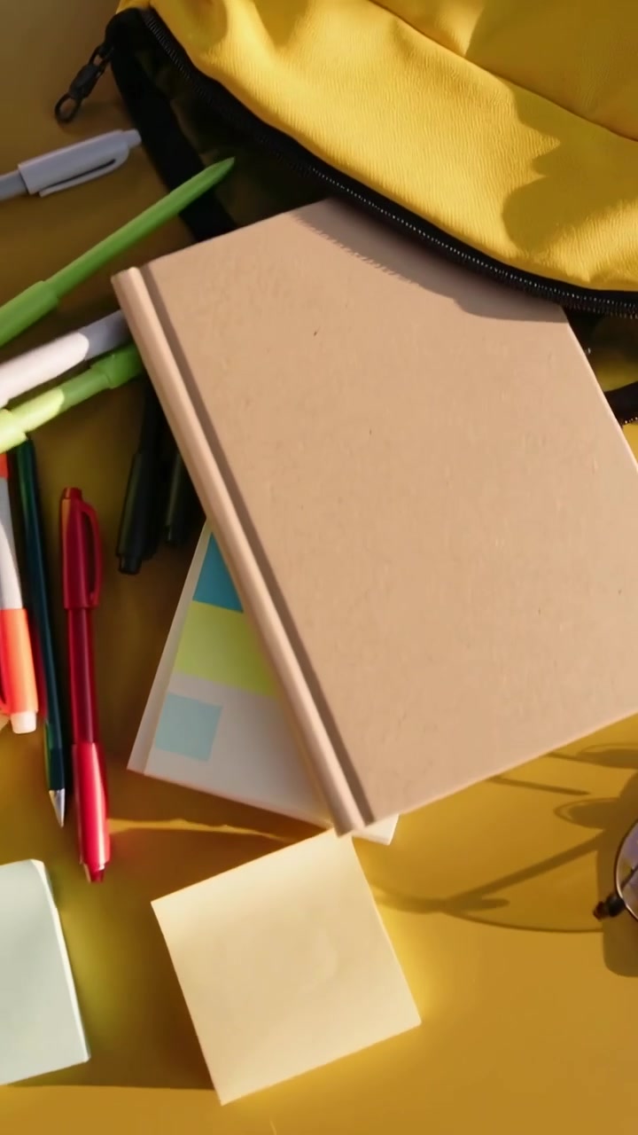 Vertical video: Unzipping pocket, yellow backpack spilling pens, notes, glasses on table for study