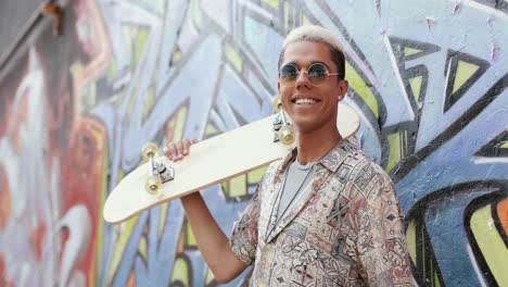 foto de retrato de un joven con estilo en estilo hipster y gafas de sol mirando a la cámara en la calle mientras sostiene una patineta