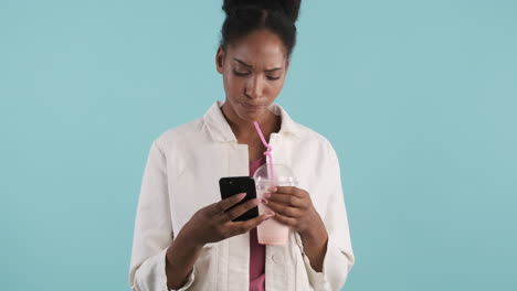 african american woman typing on phone while drinks milkshake