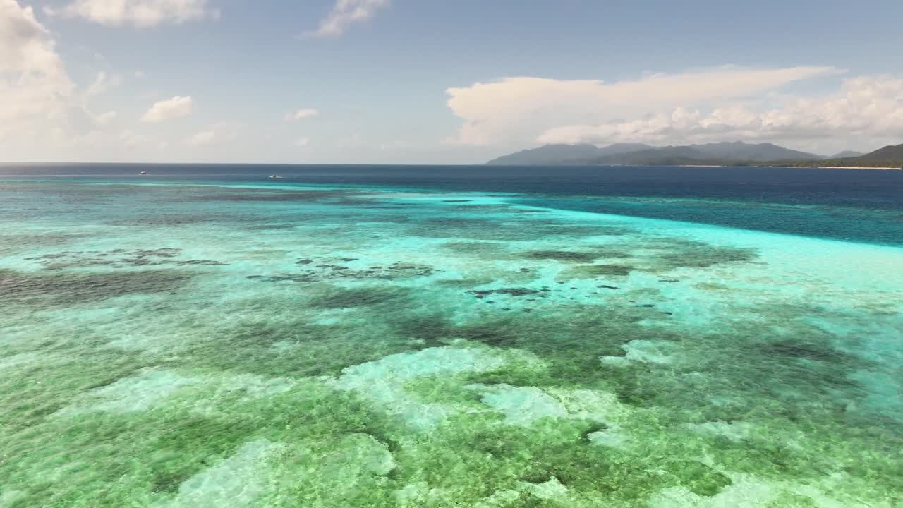 Drone view of Candaraman Sand Bar in Balabac, Palawan, revealing vibrant coral reefs beneath clear turquoise water, with distant islands and lush silhouettes under a bright sky