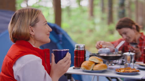 grupo de amigas en vacaciones de campamento en el bosque cocinando comida sentados en una tienda de campaña juntos