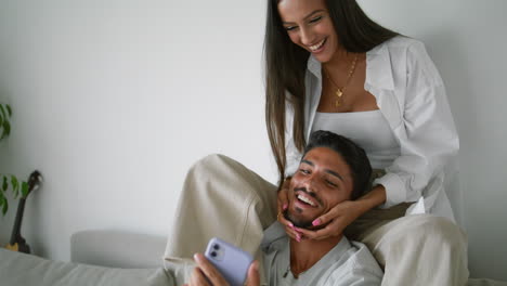 laughing woman kissing husband at couch closeup. married couple watching mobile