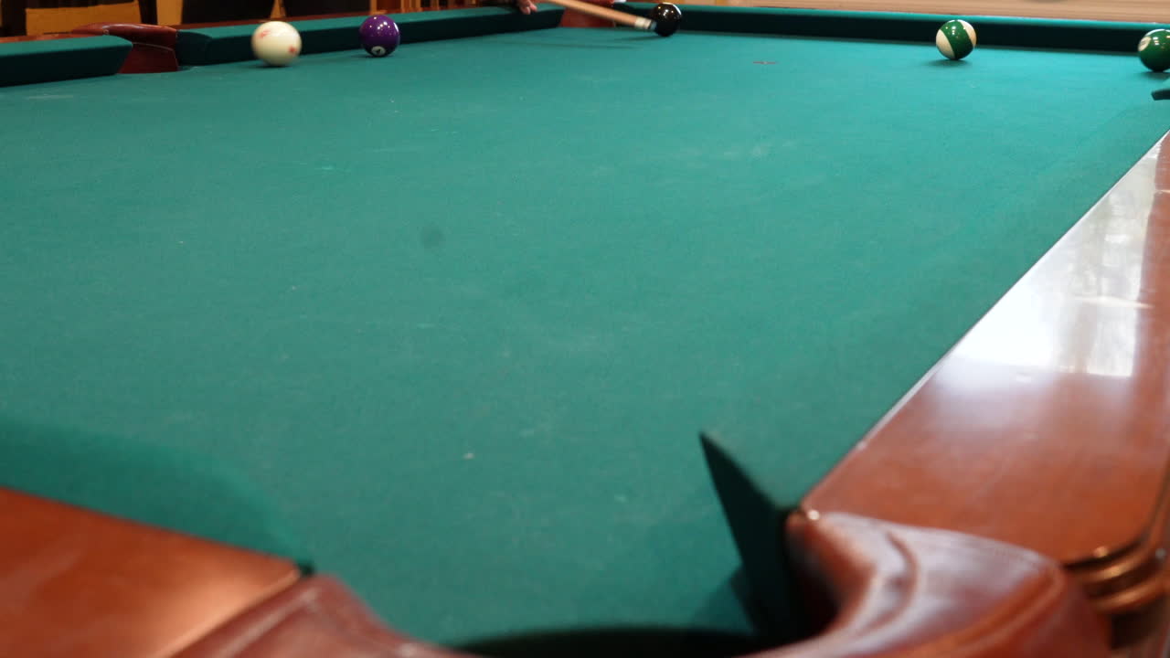Man Playing 8 Ball Pool Scratches Cue Ball in the Side Pocket on a Brunswick Table with Green Felt and Several Balls Left on the Table, Open Bridge Hand and Wooden Cue Stick, Low Angle no faces