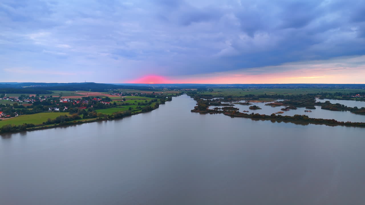 Vista aerea di un fiume e della campagna al tramonto. Vista aerea con drone di un fiume calmo circondato da campi verdi e villaggi durante un tramonto variopinto