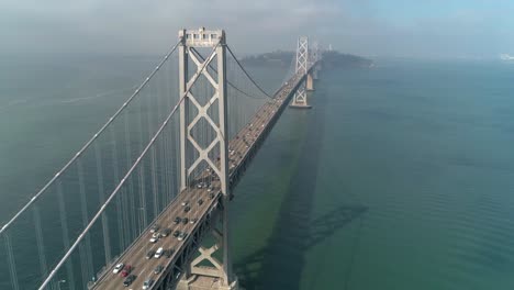 Toma-Aérea-De-Vehículos-Moviéndose-En-El-Puente-De-La-Bahía-De-San-Francisco–oakland-Con-La-Ciudad-Al-Fondo