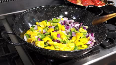 hand-held shot of a chef stirring up the freshly cut vegetables in a metal pan