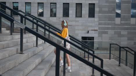 portrait of young cute attractive young girl in urban city streets background listening to music with headphones. woman wearing yellow blouse and silver skirt