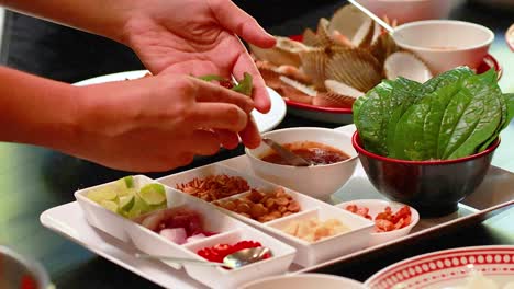 hands assemble miang kham with fresh ingredients on a table in phuket. bright lighting highlights the vibrant colors and textures