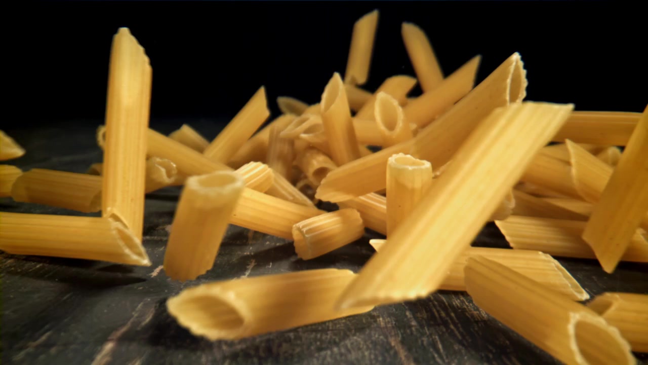 Penne Nudeln fallen in Zeitlupe auf eine dunkle Oberfläche