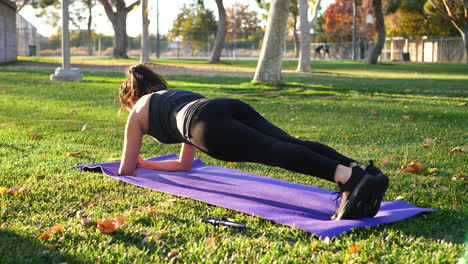 a young woman doing a plank working out her abs and core muscles on a yoga mat in slow motion in a park