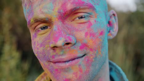 Close-up portrait of attractive guy tourist with colorful face smiling at Holi celebration
