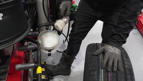 Car-mechanic-putting-tire-mounting-liquid-lube-on-aluminum-alloy-wheel,-prepping-it-for-fixing-a-tire