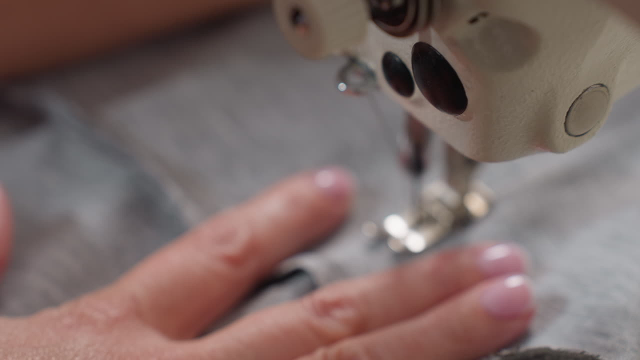 Seamstress hand pushing fabric under needle as it pierces material, controlling tension, ensuring precise stitching, focusing on alignment, showcasing expertise, finishing garment with skill