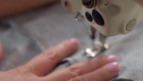 seamstress hand pushing fabric under needle as it pierces material, controlling tension, ensuring precise stitching, focusing on alignment, showcasing expertise, finishing garment with skill