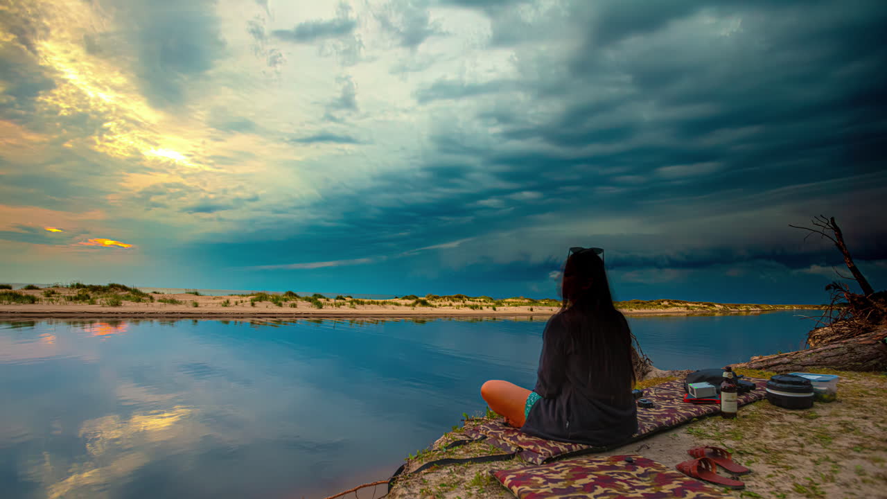 Time-lapse of dramatic beach sunset with vibrant cloudscape and two-person picnic