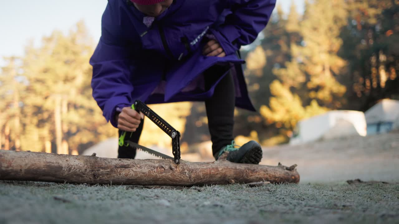 A man dressed in a heavy winter jacket, surrounded by a cold, rustic environment, cutting a wooden log using a see saw cutter, showcasing outdoor survival skills, self-reliance.