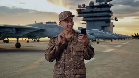 military personnel using smartphone on aircraft carrier deck at sunset