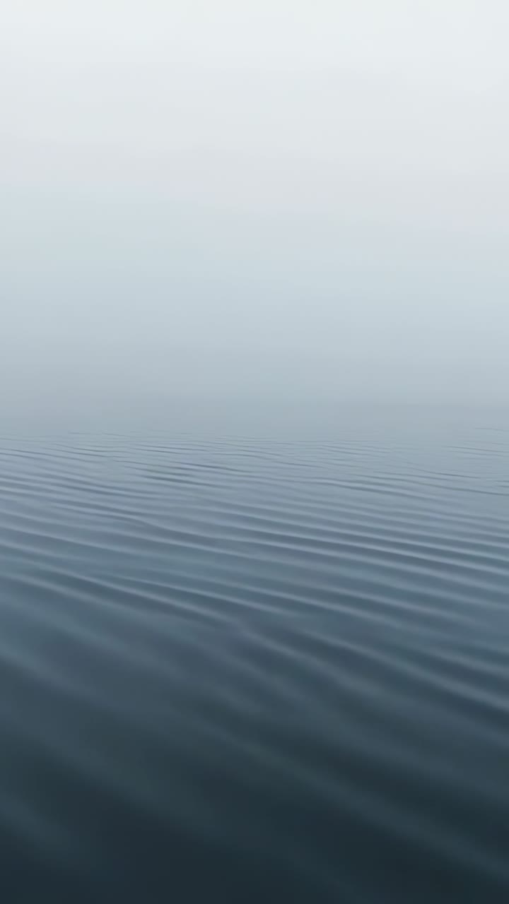 Vertical video: Moving calm rippled water surface shifting forward on open water, from light breeze