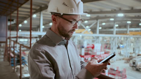 engineer in hard hat typing message on smartphone in industrial factory