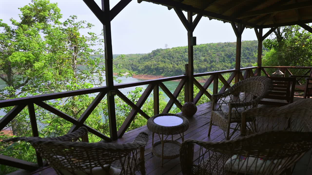 Deck with wicker chairs and glass table overlooks lush jungle and the Paraná River, with Paraguay visible across the water—captured from Argentina in a tranquil, nature-immersive setting