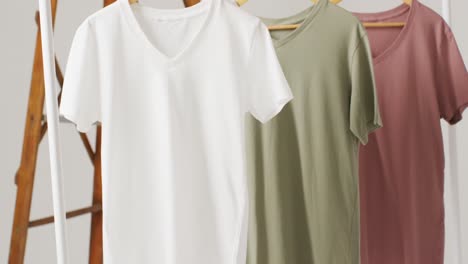 video of close up of white, beige and gren t shirts hanging on white background