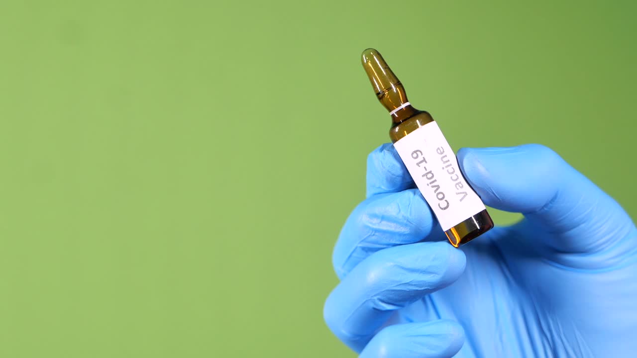 médico con guantes sosteniendo la vacuna contra el coronavirus en fondo verde