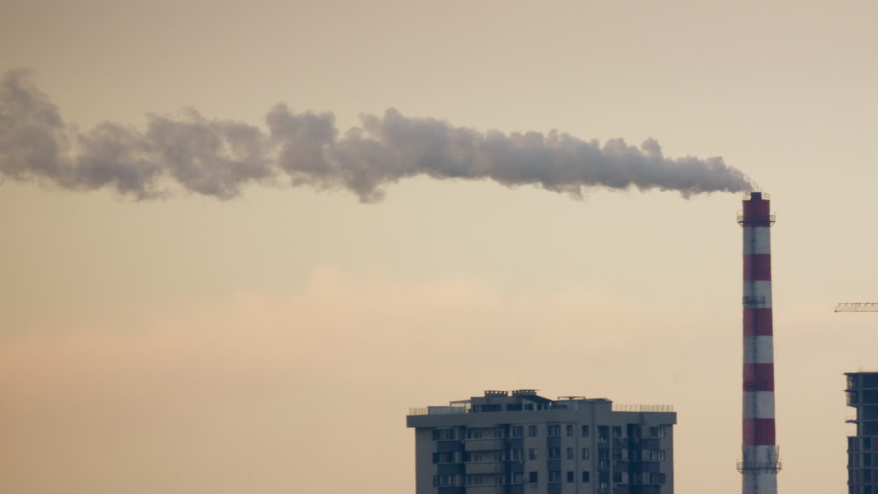 Urban skyline with residential buildings and an industrial chimney emitting smoke at sunset