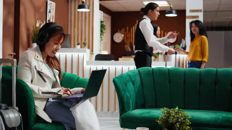 una mujer asiática disfrutando de una película en una computadora portátil en el salón del hotel.