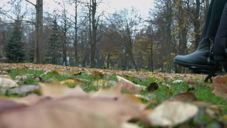 Nahaufnahme-Der-Beine-Und-Des-Rollstuhls-Einer-Behinderten-Gelähmten-Person,-Die-Sich-Auf-Dem-Boden-Des-Herbstparks-Bewegt