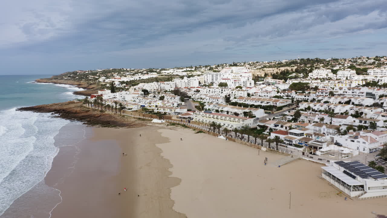 Aerial of Beach Town Luz with white buildings, sandy beach with rocks along the ocean