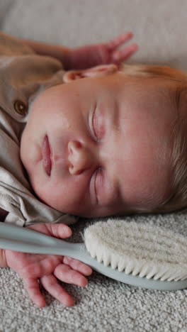 lovely cute newborn baby with blond hair lies sleeping. a hairbrush lies in the hand of a kid. close up. vertical video