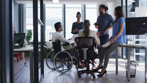 grupo diverso de colegas de trabajo hablando en una reunión casual de oficina, uno en silla de ruedas