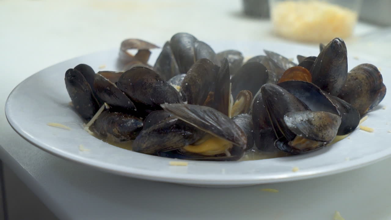 Queso parmesano rallado espolvoreado sobre un plato terminado de mejillones al vapor, primer plano HD.