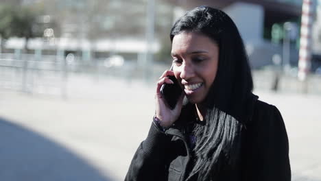 mujer joven morena sonriente hablando en el teléfono inteligente al aire libre