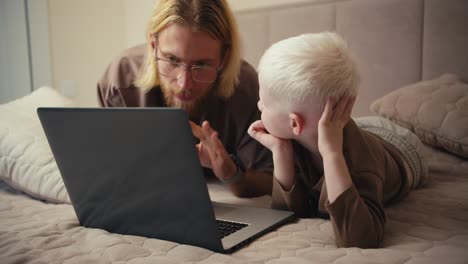 Ein-Glücklicher-Albinojunge-Mit-Weißem-Haar-Schaut-Seinen-Vater-An,-Während-Er-Einen-Lehrfilm-Sieht,-Und-Stellt-Ihm-Eine-Frage.-Der-Mann-Antwortet-Seinem-Jungen-Und-Versucht,-Alle-Seine-Fragen-Zu-Klären