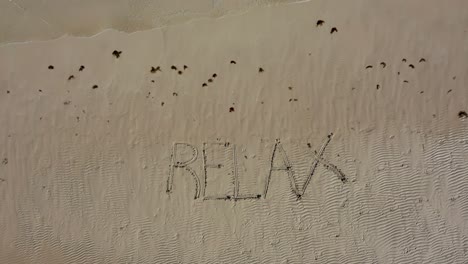 Aerial-camera-descending-onto-RELAX-inscribed-into-the-sand-on-a-beach