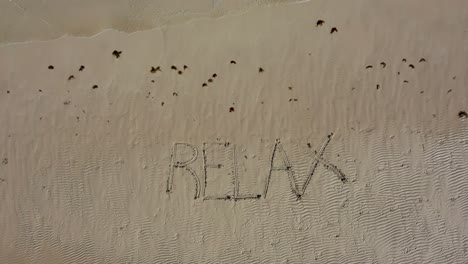 aerial camera descending onto relax inscribed into the sand on a beach