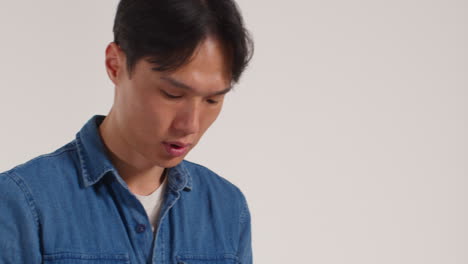 색 스튜디오 배경 앞에 휴대전화를 들고 있는 남자가 사진 부스 스타일의 초상화를 위해 포즈를 취하고 있다.
