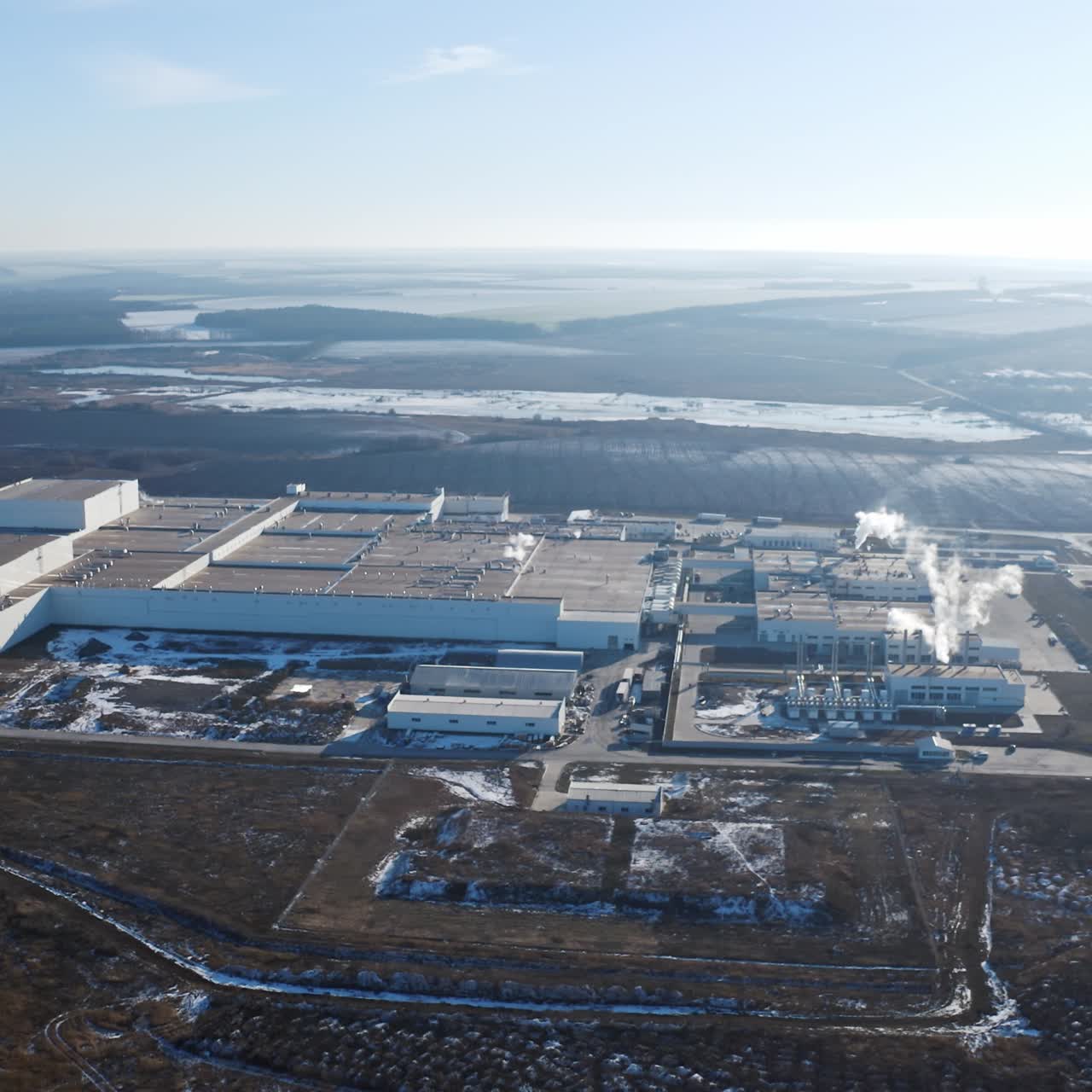 Huge industrial plant among nature. View from the air on a modern factory surrounded by fields and forests in winter time. Aerial view.