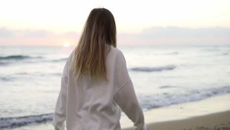 happy woman walking along ocean coast in white suit, smiling and spinning around