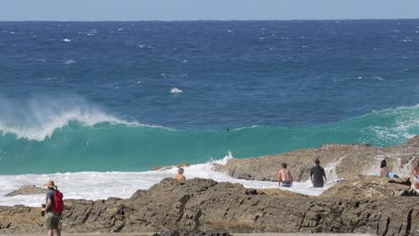 spectators watch as waves hit a rocky coastline