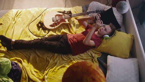 teenager relaxing in bedroom with guitar and phone