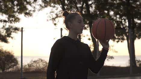 hermosa chica con capucha negra girando una pelota de baloncesto en su dedo al aire libre