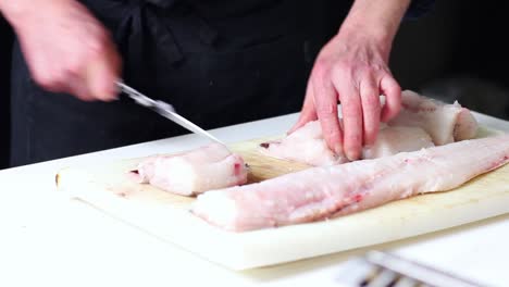 un pescadero limpiando una merluza, haciéndola porciones para el restaurante