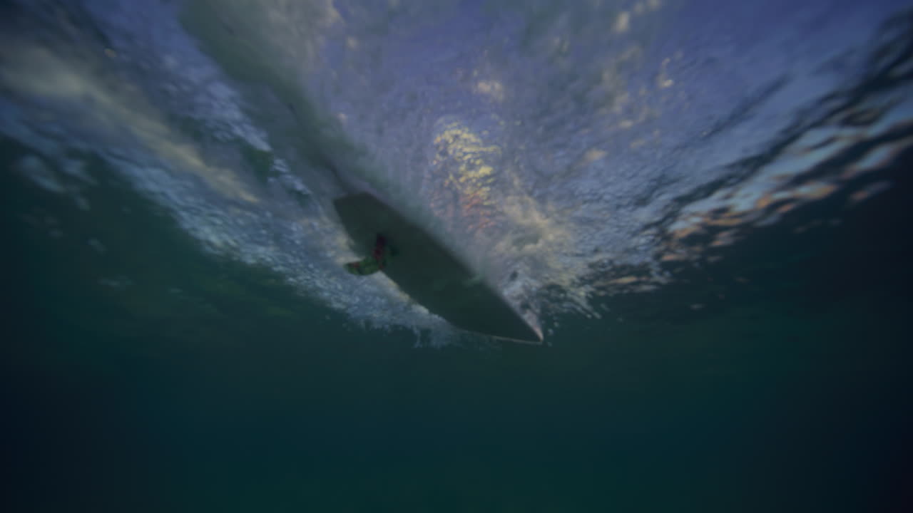Vista subacquea posteriore di un surfista su longboard che scivola su un'onda che si infrange