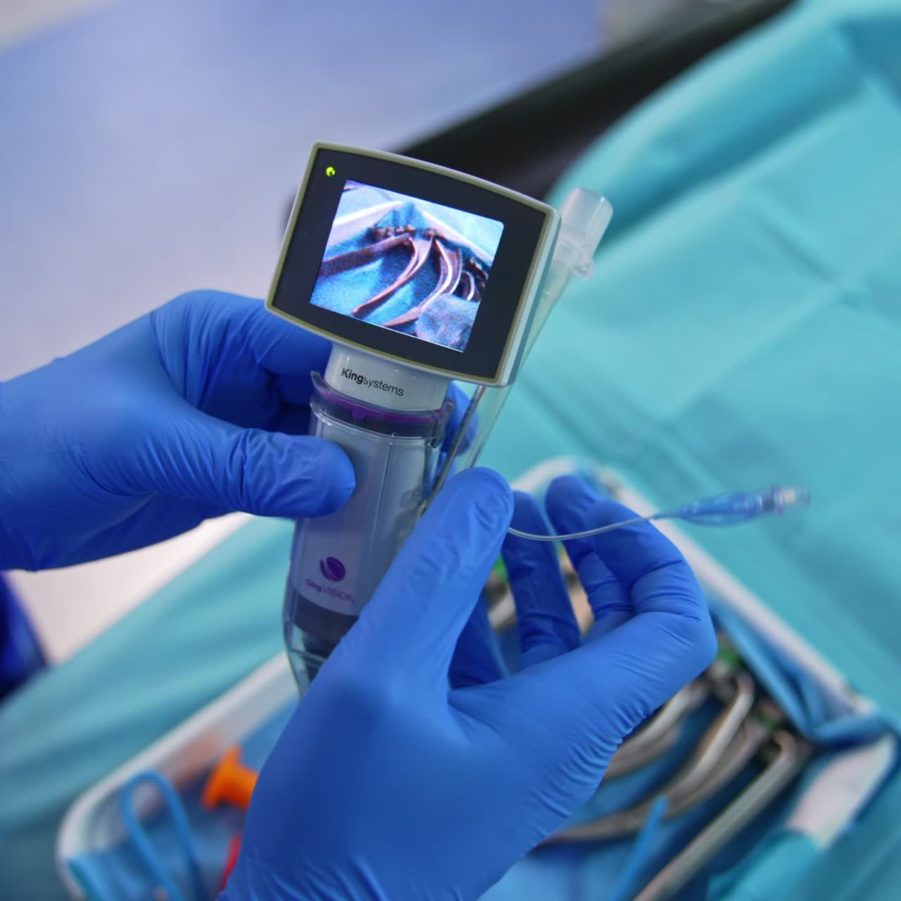Gloved hands of a medic holding a portable video laryngoscope. Doctor presses the button and little screen switches on. Close up
